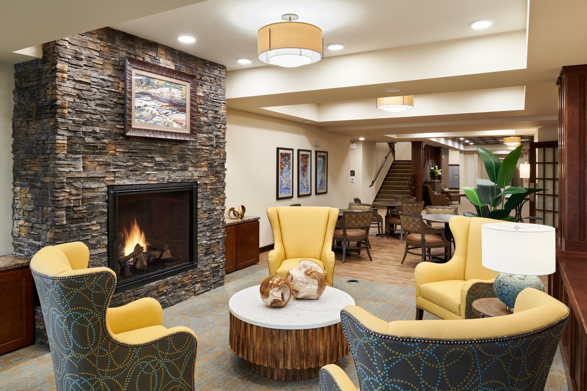 A cozy and modern living room with a fireplace, featuring yellow chairs and wood accents.