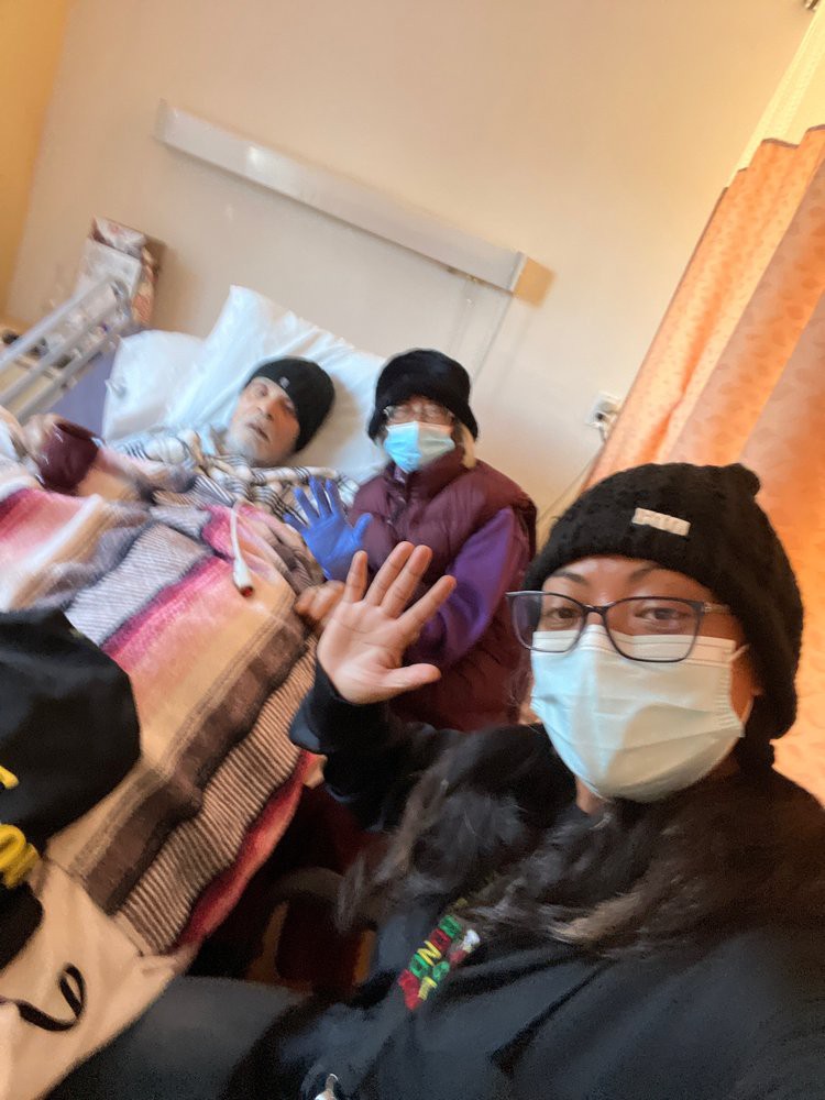 Family members visit a patient in the hospital, all wearing masks.