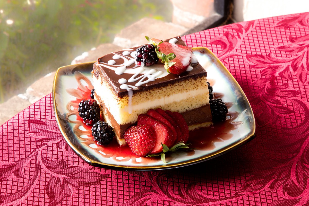 A decadent layered dessert topped with chocolate and adorned with fresh berries served on an ornate plate.