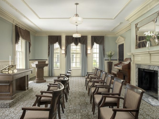 A quiet meeting room with arranged chairs, a lectern, and large windows with curtains.