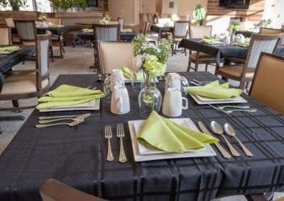 An elegantly set dining table in a restaurant with green napkins and floral centerpiece.