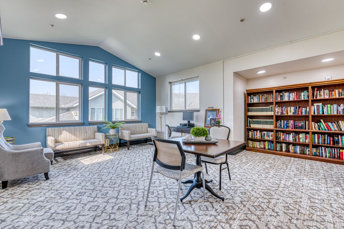 A modern living room with large windows, comfortable seating, and a bookshelf.