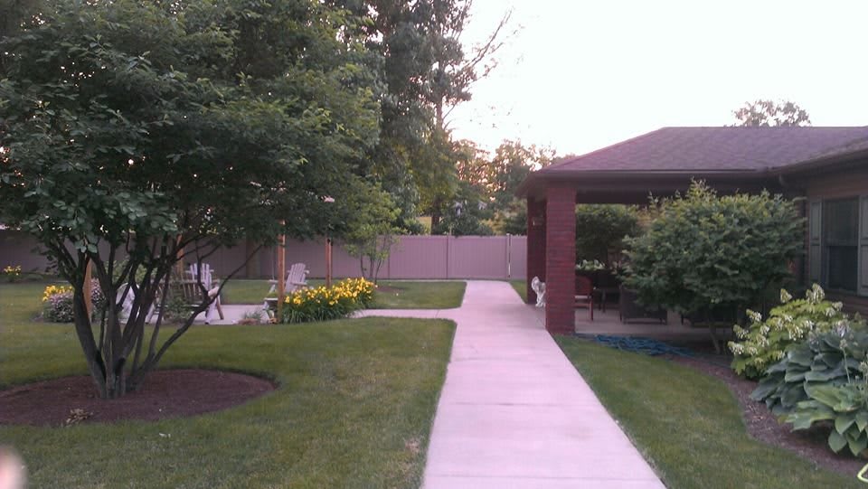 A tranquil garden with a paved pathway leading to a gazebo, surrounded by trees and flowers.