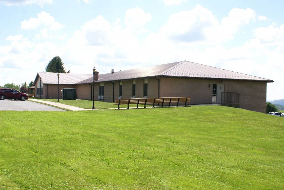 A single-story brick building surrounded by a green lawn under a partly cloudy sky.