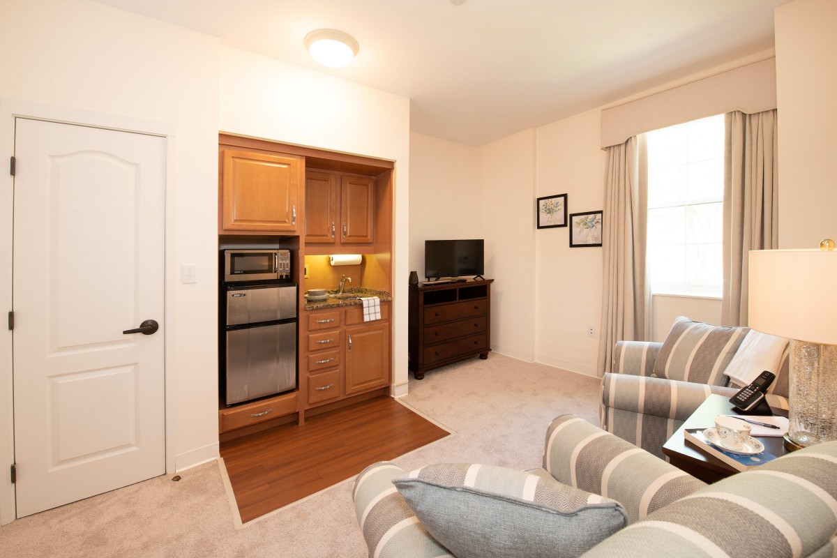 A cozy living area with a kitchenette, featuring striped armchairs and a television.