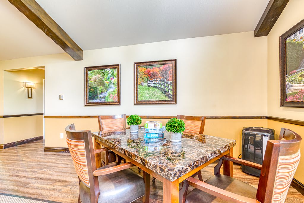 A cozy dining area with a marble top table, surrounded by wooden chairs and decorated with small plants and framed artwork.