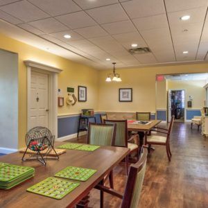 A cozy dining room with neatly arranged tables and chairs, featuring warm lighting and wooden floors.