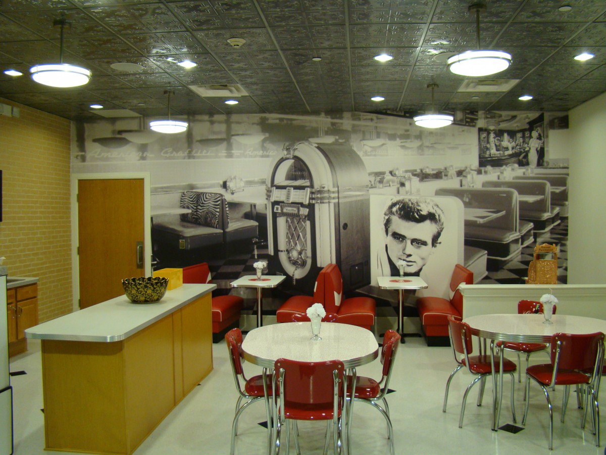 A retro-themed diner with red chairs and a vintage jukebox mural on the wall.