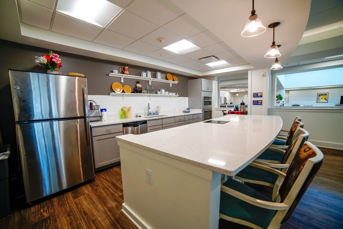 A modern kitchen interior featuring stainless steel appliances and a large white countertop with bar stools.