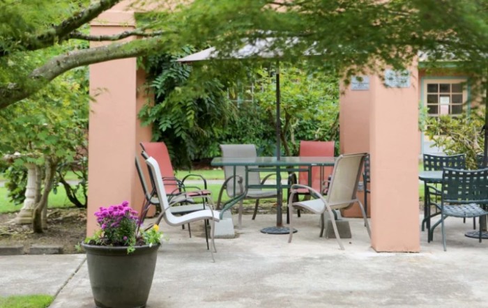 An inviting patio setup with a table, chairs, and umbrella surrounded by lush greenery.