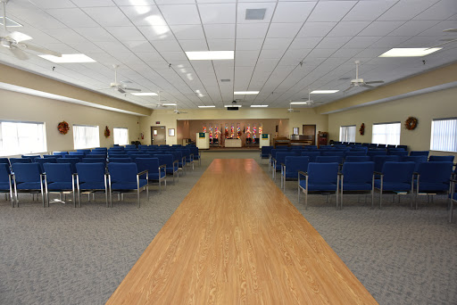 A spacious empty hall with blue chairs arranged in rows, leading towards a stage area.