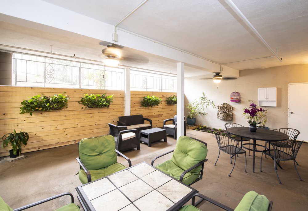 A cozy indoor patio with comfortable seating, green cushioned chairs, and plants adorning the walls.