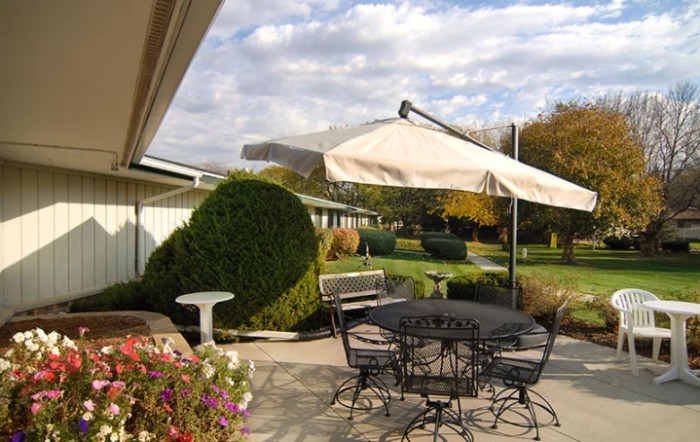 A peaceful patio setting with a table, chairs, and umbrella overlooking a well-maintained garden.