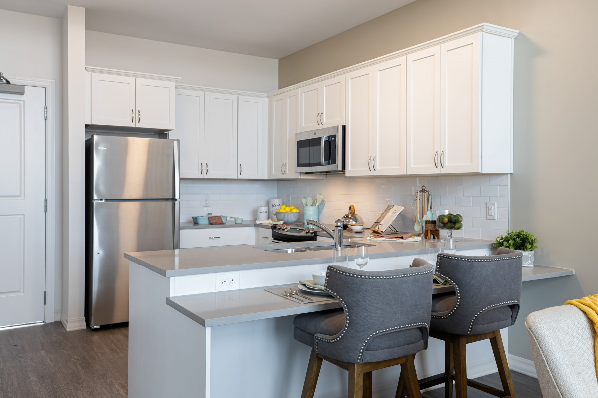 A modern kitchen with white cabinets, stainless steel appliances, and a stylish countertop with bar stools.