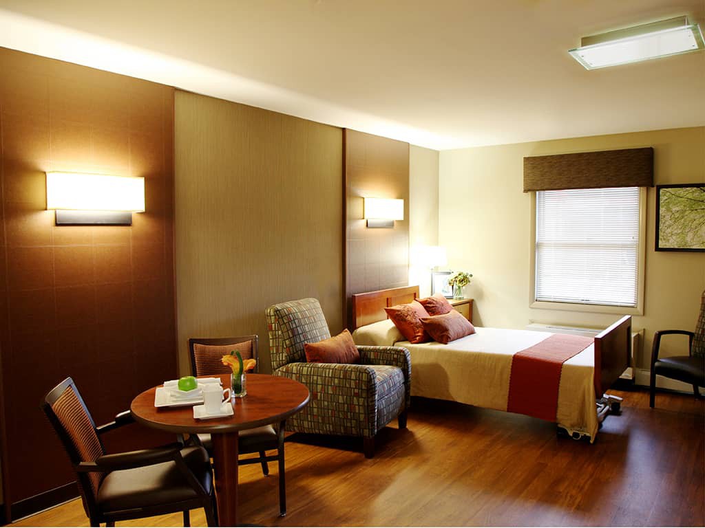 A well-lit hotel room featuring a comfortable bed, armchair, and dining area.