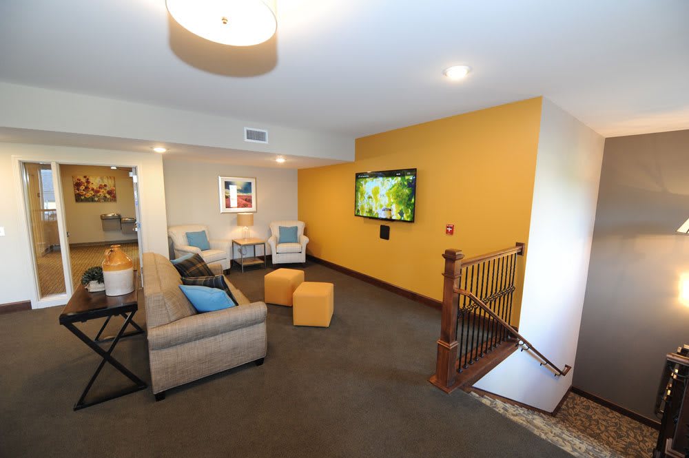 A modern living room with a comfortable sofa, chairs, and a wall-mounted television on a yellow accent wall.