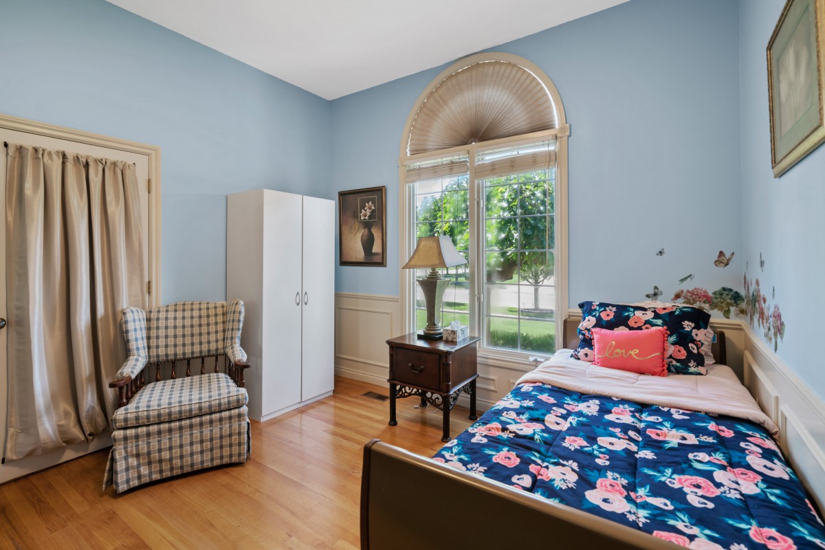 A cozy bedroom with blue walls, a floral bedspread, and large arched windows allowing natural light to fill the room.
