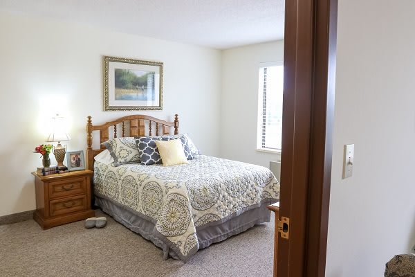 A cozy bedroom with a neatly made bed, wooden furniture, and a framed painting on the wall.
