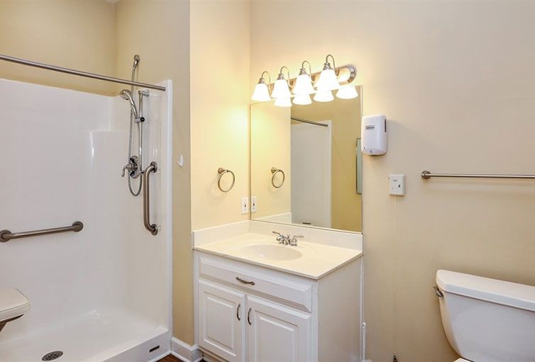A clean and well-lit bathroom with a shower, vanity with a sink, mirror, and overhead lighting.