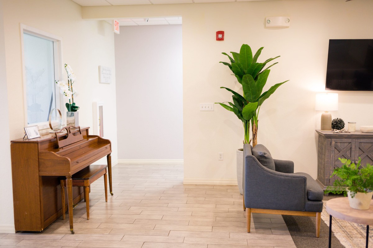 A minimalist waiting room with a piano, plant, and a gray sofa.