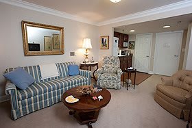 A cozy living room featuring a striped sofa, floral armchair, wooden coffee table, and decorative elements like a mirror and lamp.