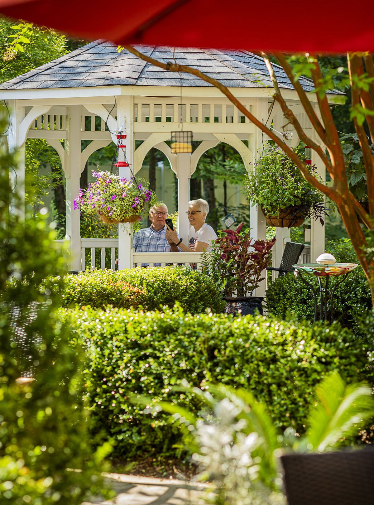 Two elderly people enjoying a peaceful moment in a garden gazebo surrounded by lush greenery.