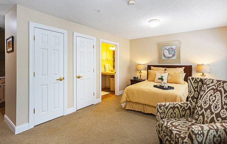 A cozy bedroom featuring a neatly made bed with neutral-colored bedding, decorative pillows, and wall art. The room includes two closets and an adjacent bathroom.