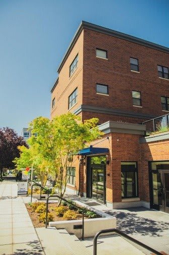 A sunny day view of a brick building with trees and a sidewalk in the foreground.