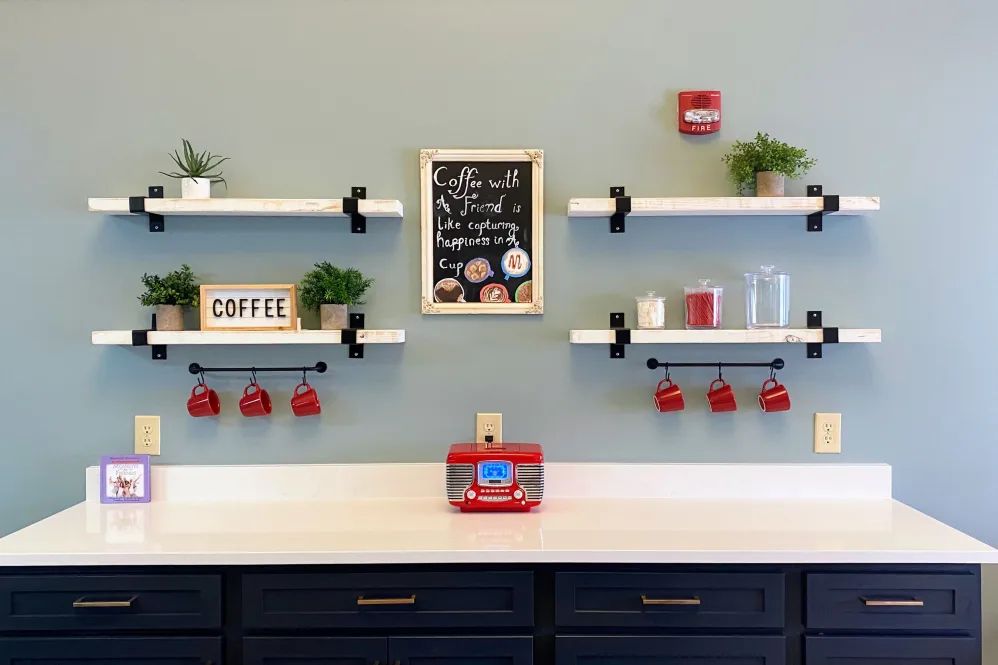 A stylish coffee station with shelves, red mugs, and decorative plants against a light blue wall.