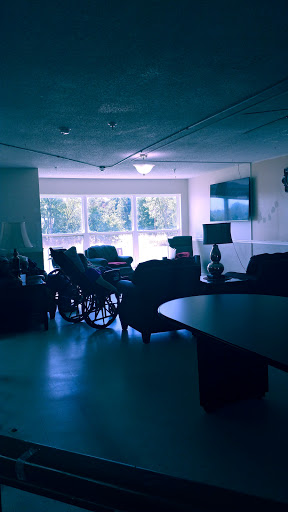 A cozy indoor living space featuring a wheelchair, comfortable seating, and ample natural light from large windows.