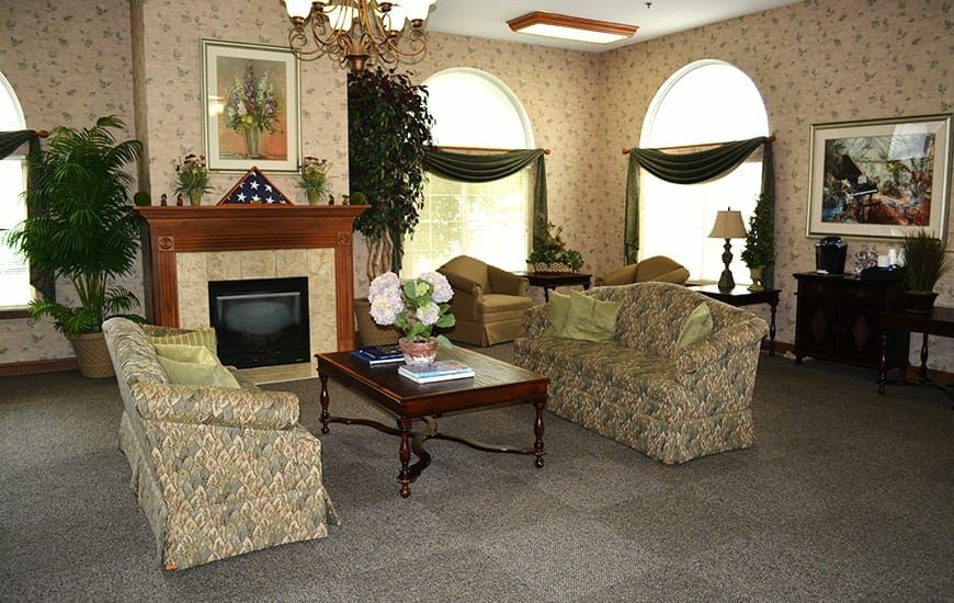 A cozy living room with classic decor, featuring floral sofas, a fireplace, and large arched windows.