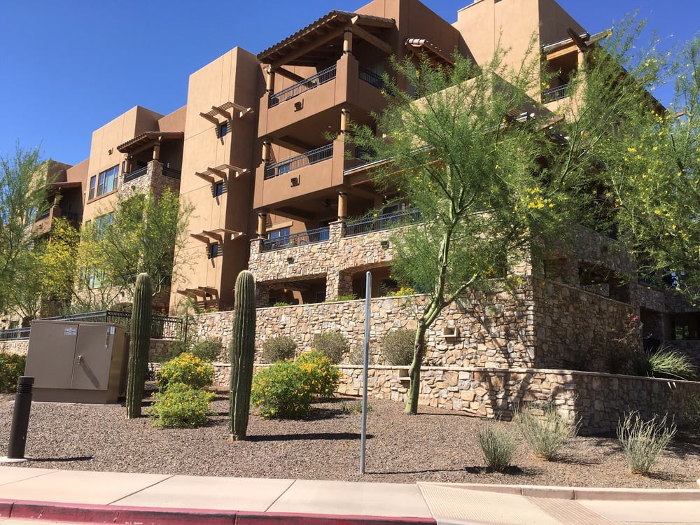 A modern apartment building with desert landscaping featuring cacti and stone walls on a sunny day.