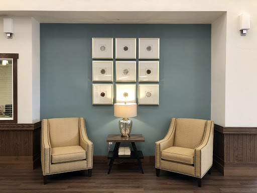 A cozy seating area featuring two beige chairs, a stylish lamp, and decorative wall art.