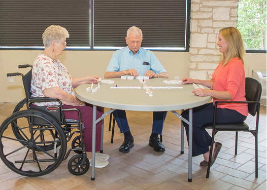 Three people sitting around a table, one in a wheelchair, engaged in an indoor meeting.