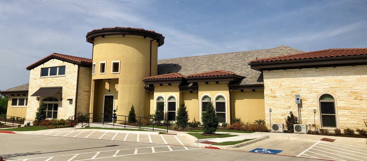 A view of a modern commercial building with Mediterranean-style architecture, featuring a curved facade and landscaped surroundings.