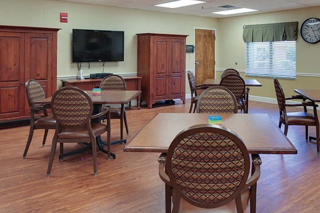 A community room with tables, chairs, a television, and a wooden cabinet.