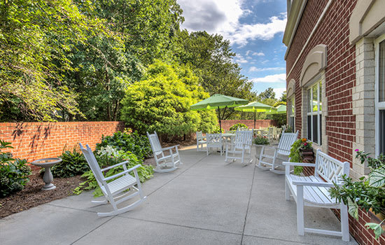 A peaceful patio area with white rocking chairs and a large umbrella, surrounded by lush greenery.