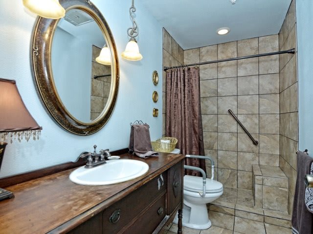 A well-appointed bathroom featuring a wooden vanity with a round mirror, tiled shower area, and modern fixtures.