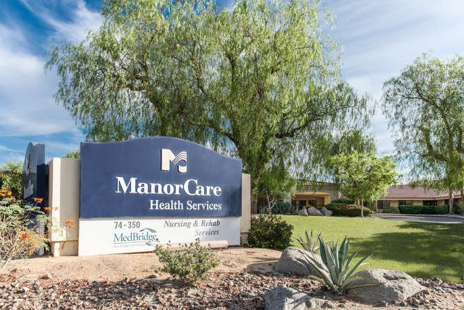 Sign for ManorCare Health Services surrounded by greenery.