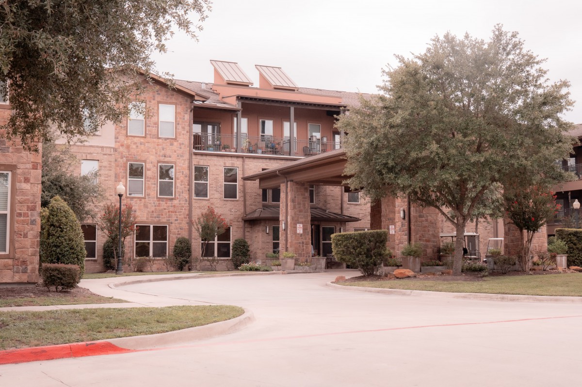 A residential building with a brick exterior, surrounded by trees and a driveway in front.