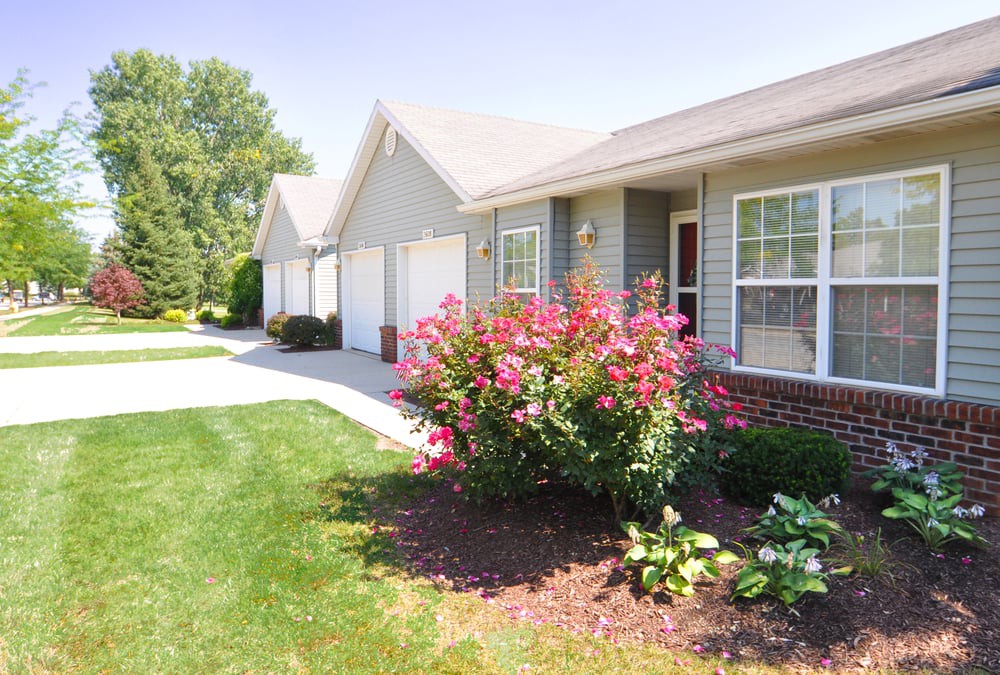 A suburban house with a well-maintained garden and bright pink flowers along the driveway.