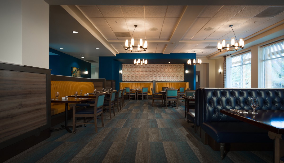 A modern restaurant interior featuring elegant chandeliers, a blue and yellow color scheme, and neatly arranged tables and chairs.
