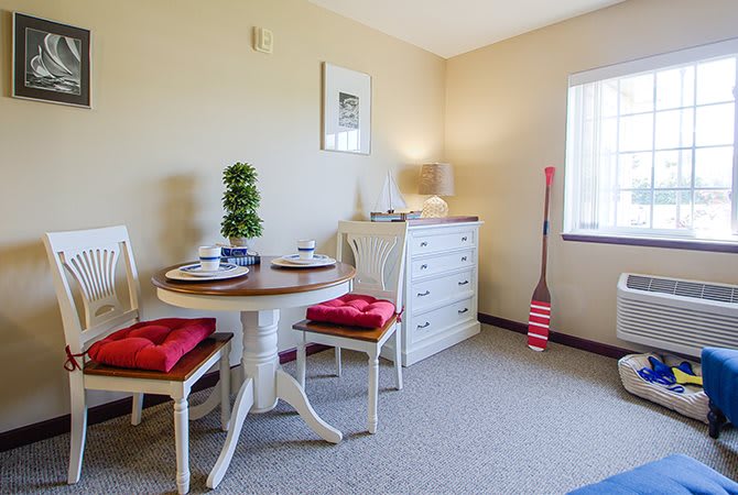 A cozy dining area with a round table, red-cushioned chairs, and white furniture bathed in natural light.