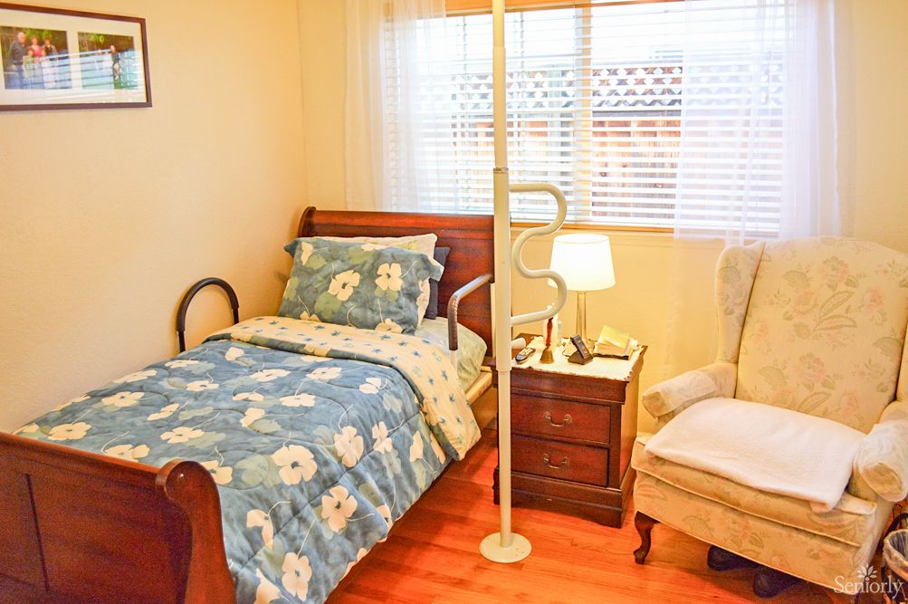 A cozy bedroom with floral bedding, a wooden nightstand, and a comfortable armchair by the window.
