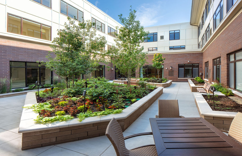 A landscaped courtyard with trees, flowers, and patio furniture surrounded by a building.