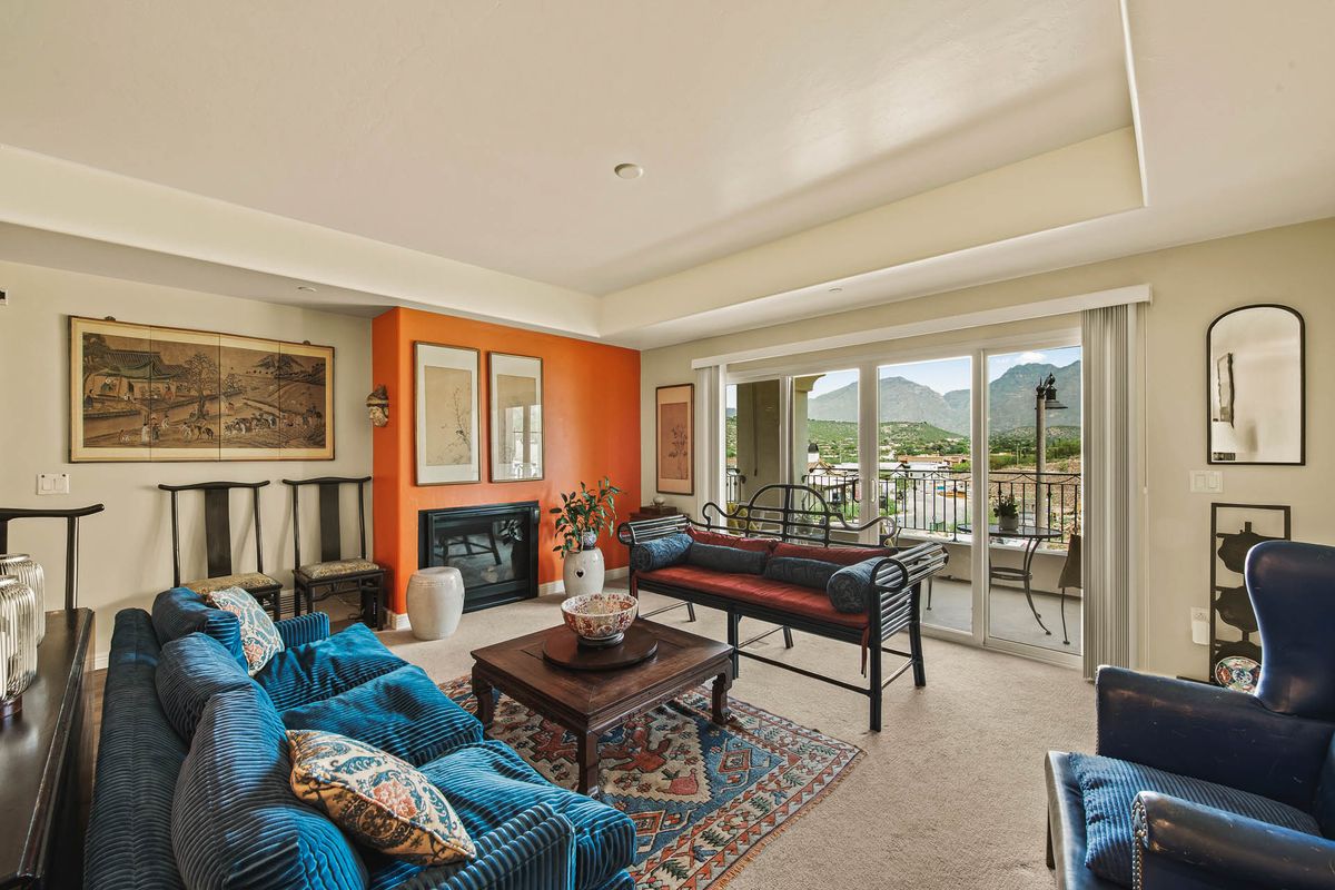 A cozy living room with an orange accent wall, stylish furniture, and large windows offering a mountain view.