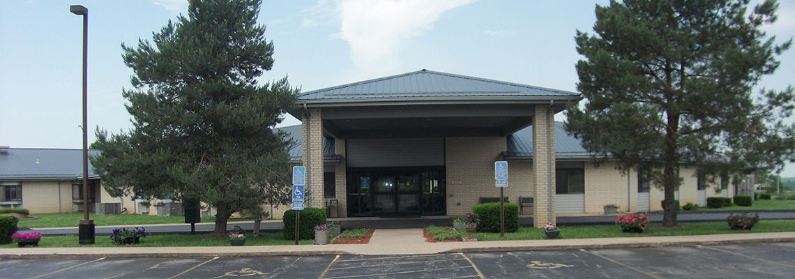 A front view of a building with a parking lot and landscaped surroundings.
