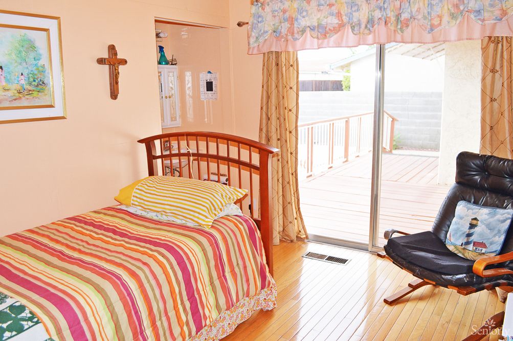 A cozy bedroom with a single bed featuring striped bedding, a cross on the wall, and a sliding glass door leading to an outdoor space.