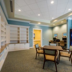 A modern conference room featuring a central table with chairs, surrounded by built-in shelves and soft lighting.