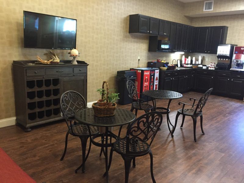 A cozy cafe area with wrought iron tables and chairs, vending machines, a television, and a potted plant on a wooden floor.